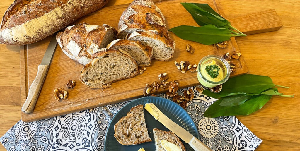 fertig gebackenes Bärlauchbrot dekoriert mit Walnüssen, Bärlauch und Butter als Aufstrich
