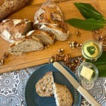 fertig gebackenes Bärlauchbrot dekoriert mit Walnüssen, Bärlauch und Butter als Aufstrich