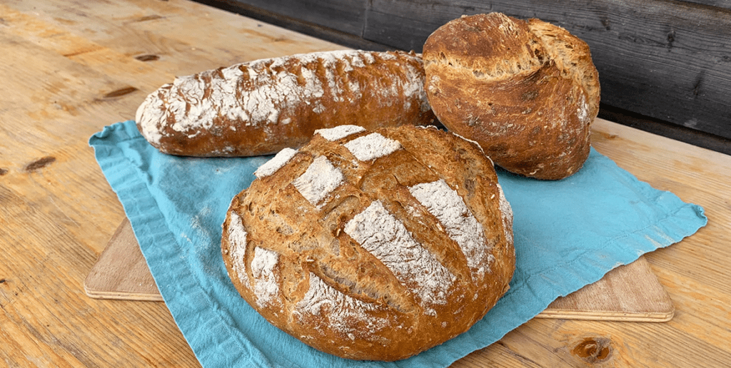 drei verschieden geformte Brotlaibe liegen auf einem blauen Tuch